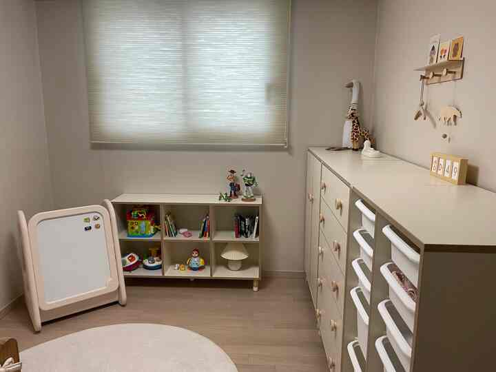 白とベージュのトーンの子供部屋、シンプルでナチュラルな雰囲気の中におもちゃ収納とブラインドが配置された空間