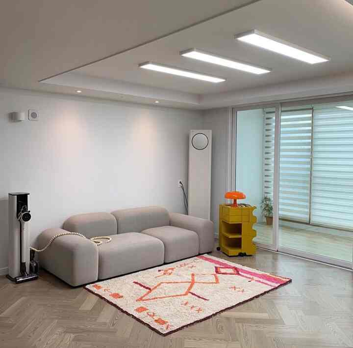 Modern living room in white and beige tones featuring a beige sofa, colorful rug, and yellow trolley with a clean aesthetic