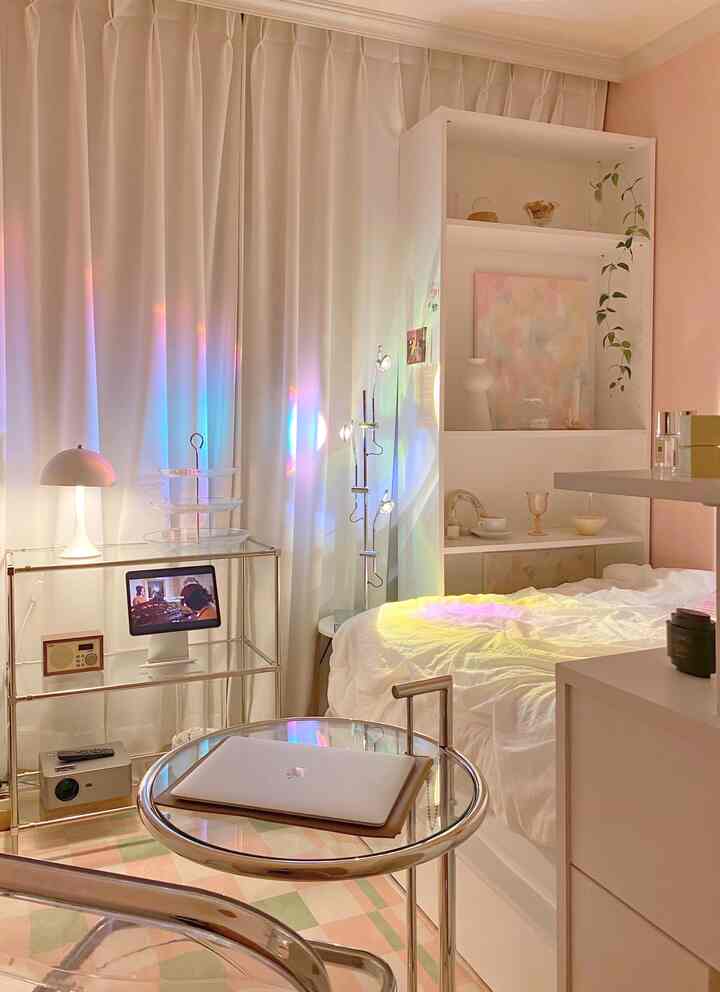 ピンクとホワイトトーンの寝室、透明なテーブルと棚、絵画が配置された落ち着いた雰囲気のあるインテリア