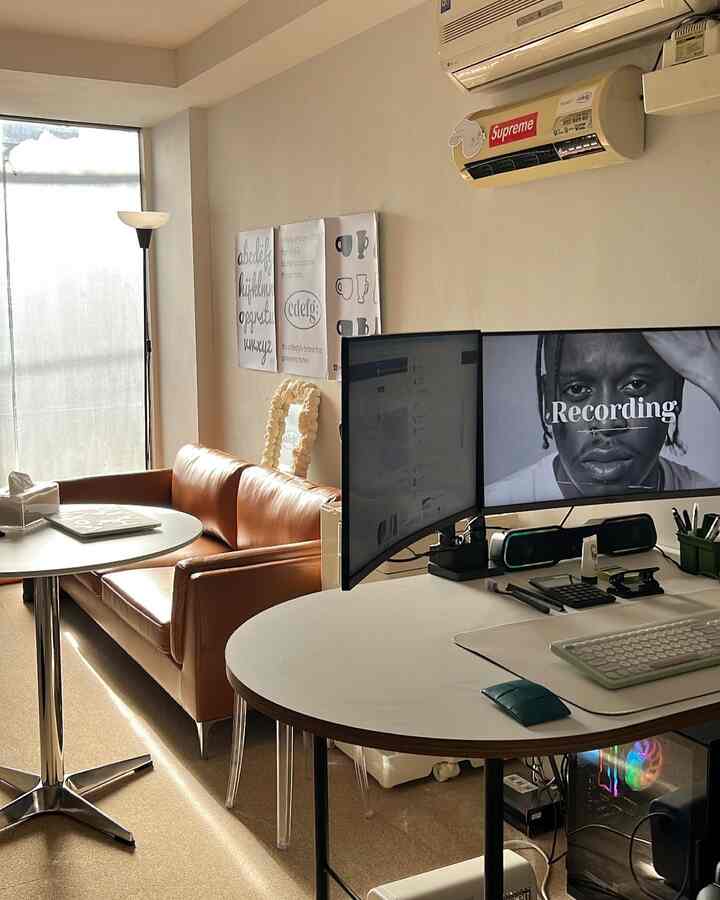 A modern home office space with white and brown tones featuring a brown leather sofa and round desks in a compact workspace