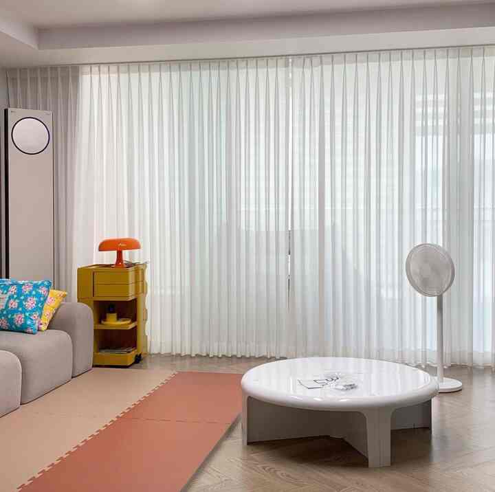 White and beige toned living room with beige sofa, white round coffee table, large windows with curtains creating a bright and airy space