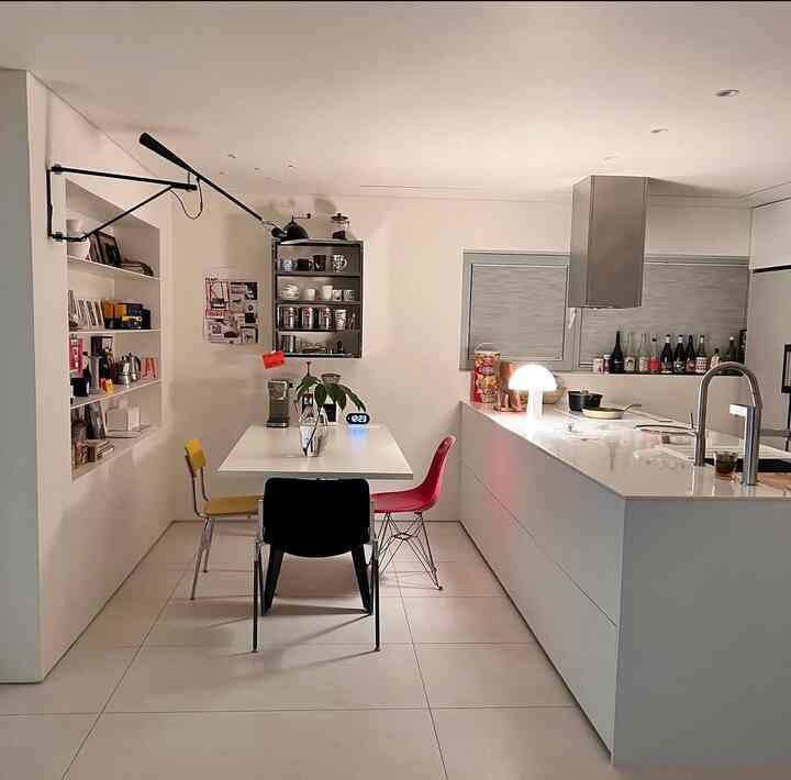 White-toned kitchen space featuring a central dining table with colorful chairs in a clean, modern interior