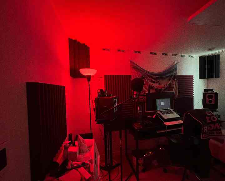 Music studio with red ambient lighting, featuring a desk with laptop and microphone, acoustic panels and speakers in a modern home office space