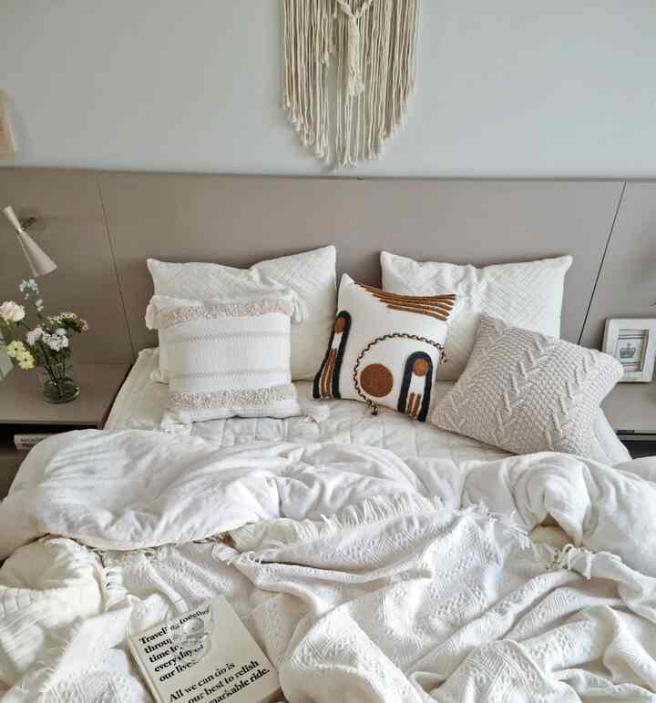白とベージュのトーンの寝室、キルティングの寝具と複数のクッションが配置された雰囲気のあるナチュラルモダンな空間