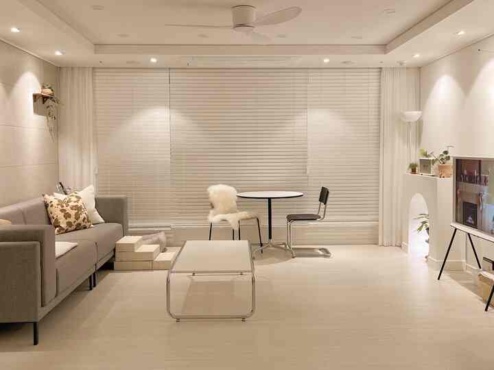 白とグレーのトーンのリビング、ミッドセンチュリーモダンのソファと落ち着いたコーヒーテーブルが配置されたミニマルな空間