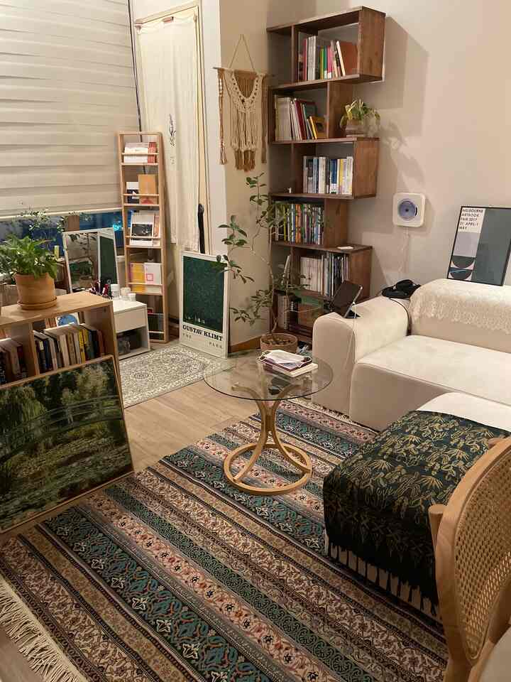 ベージュと木目調のリビング、丸型ガラスのコーヒーテーブルと本棚、多彩なカーペットと植物が配置された雰囲気のある空間