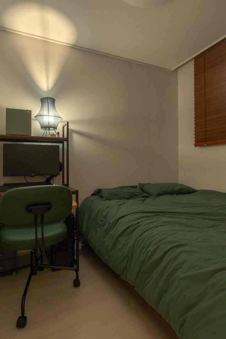 Compact bedroom in green and wood tones featuring a bed and computer desk creating a cozy atmosphere