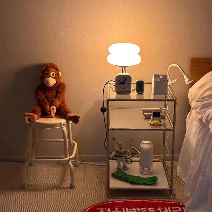 暖かいナチュラルカラーの寝室、クリーム色のスツールにオランウータンのぬいぐるみと照明が配置された落ち着いたインテリア