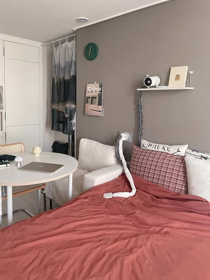 Beige-toned wall, white sofa, and red bedding in a simple modern studio bedroom with a home office setup
