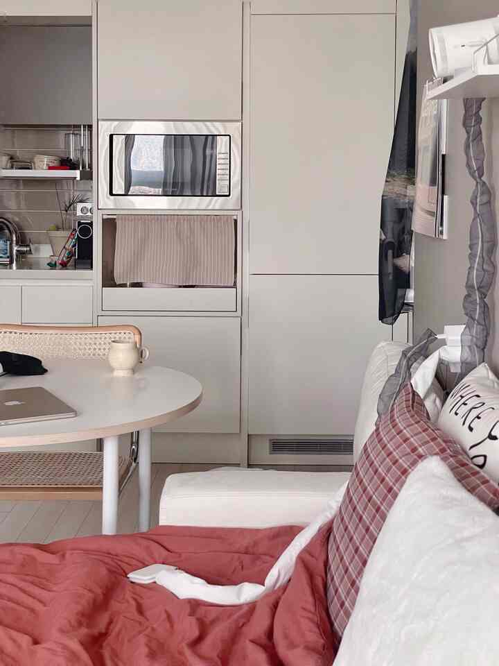 White and natural beige toned studio apartment kitchen and sofa area, creating a clean and cozy atmosphere