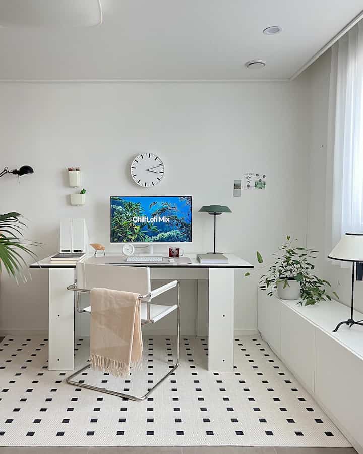 White-toned home office space featuring a desk and chair centrally placed with plants and rug creating a simple atmosphere