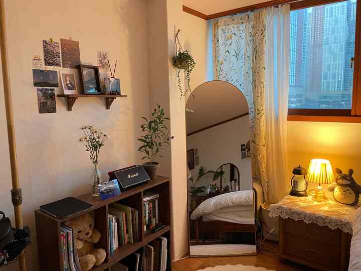 Beige walls and wood-tone furniture in a cozy bedroom featuring a large arch mirror, floor lamp, and bookshelf