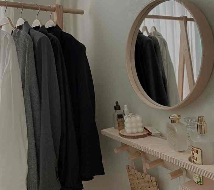 Natural wood tone studio apartment space featuring a wooden coat rack, round wooden mirror, and cube candle creating a cozy atmosphere