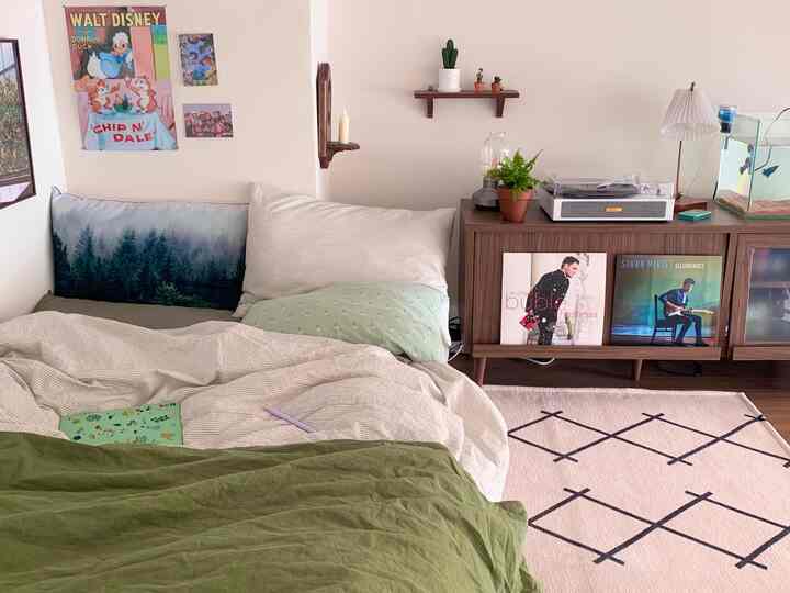 White walls and wood-tone furniture blend in a studio bedroom featuring plants and a vintage LP turntable, creating a cozy, natural atmosphere