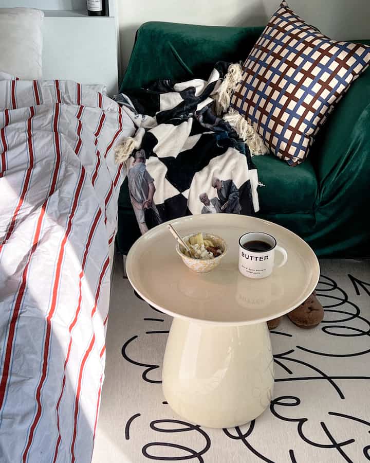 An cozy bedroom featuring an ivory simple side table, green sofa, and striped bedding