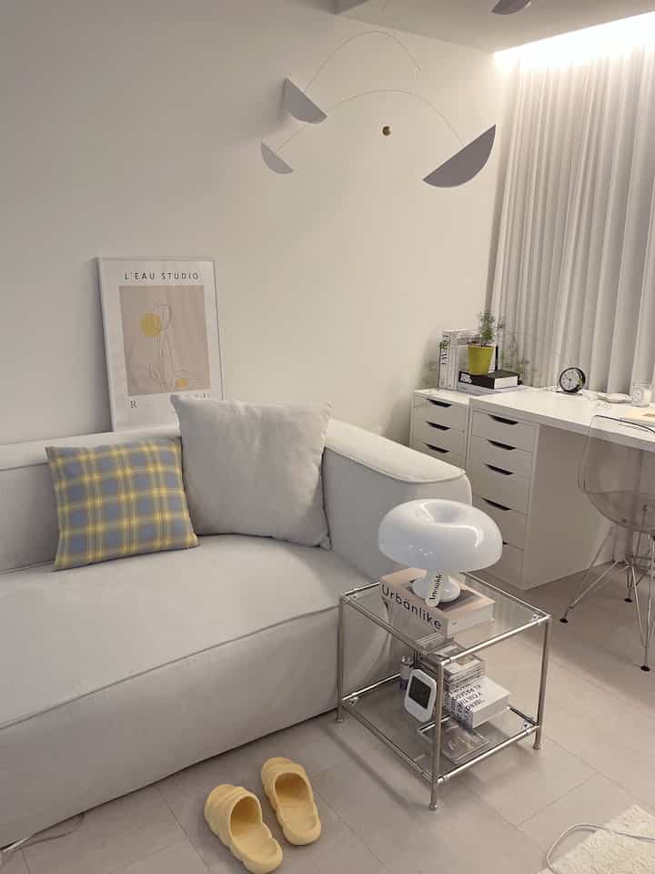 White and yellow toned living room featuring a large sofa, desk, yellow cushions and slippers in a clean setting
