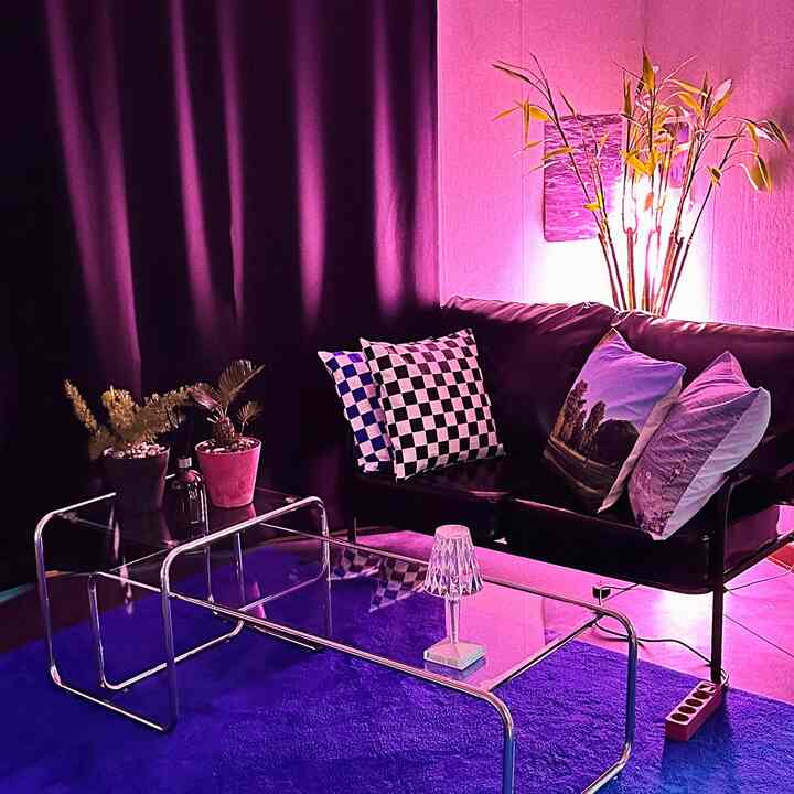 Modern living room with purple lighting, black sofa, transparent tables, and cushions