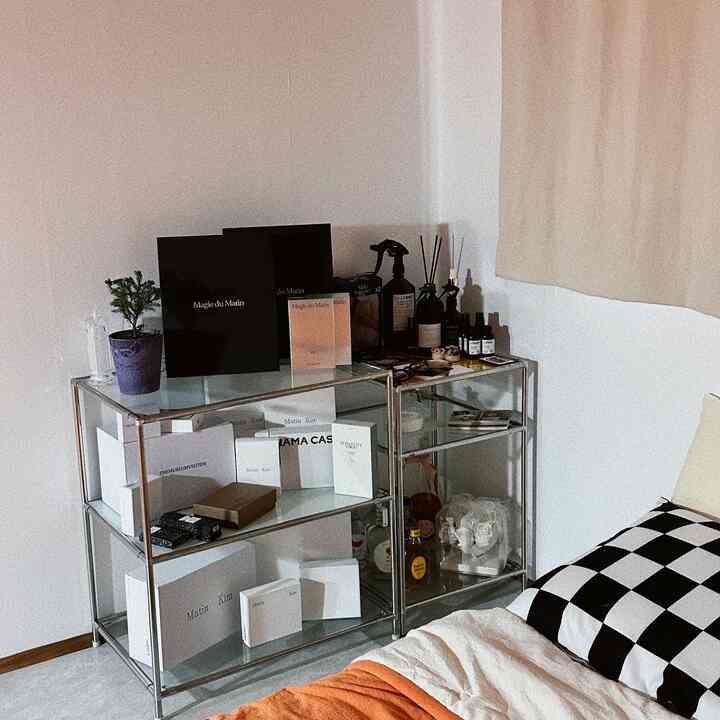 Modern bedroom with white walls and stainless steel shelf, featuring checkered pillow and curtain in a neat interior