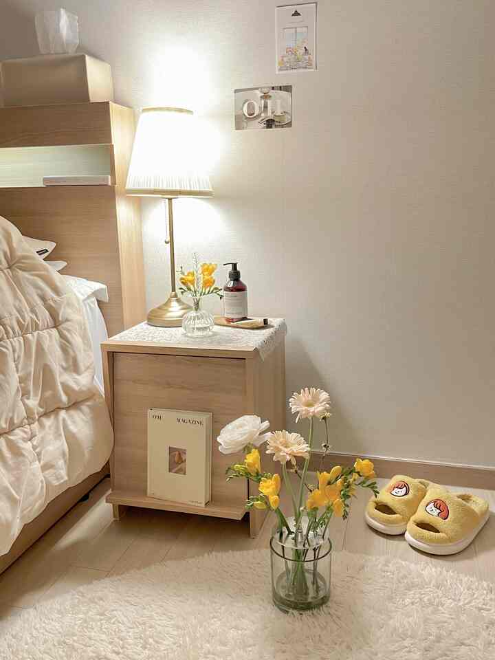 アイボリーとライトブラウンの色調の寝室、ナイトテーブルの上にテーブルランプと花瓶が置かれた雰囲気のあるインテリア
