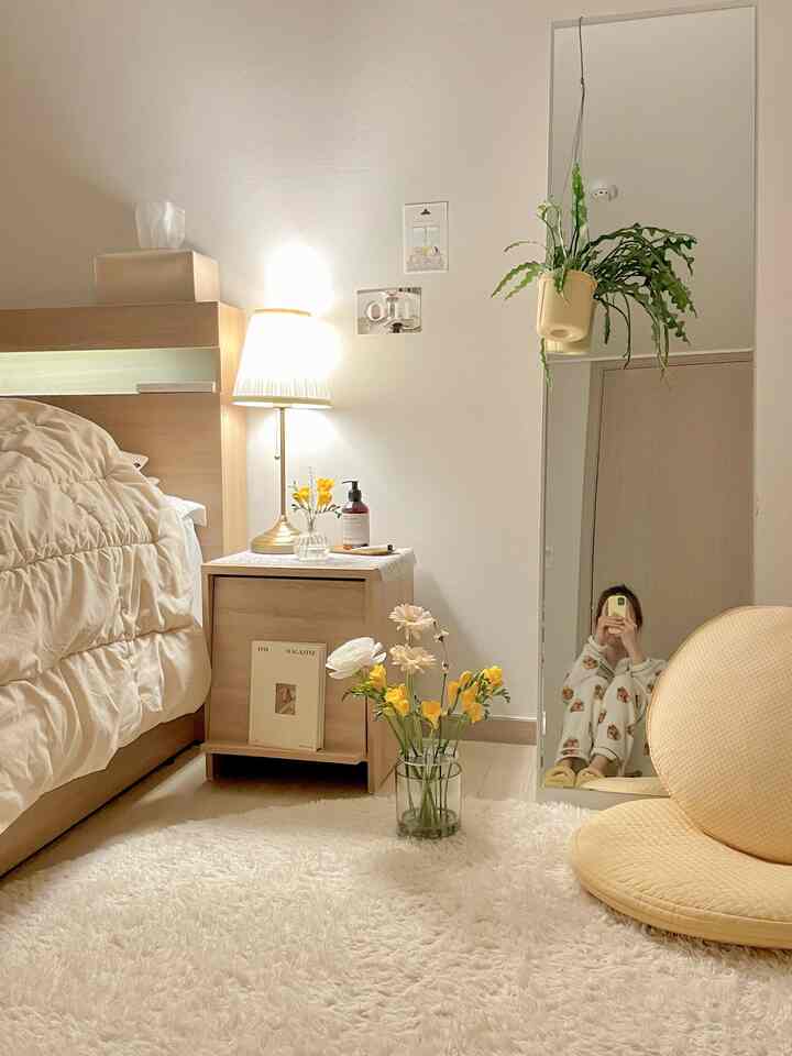 Ivory and wood tone bedroom featuring bed, nightstand, full-length mirror, and plants creating a cozy atmosphere