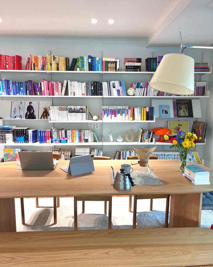 Bright white-walled Nordic dining room featuring a wooden dining table, colorful bookshelves, and coffee equipment