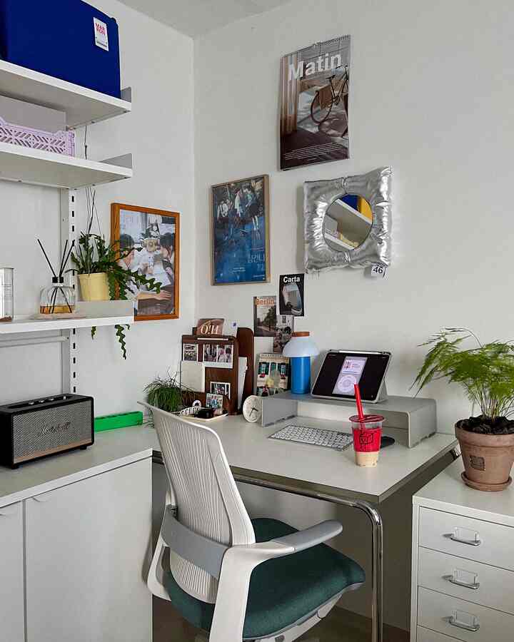 白い壁とデスクが配置されたナチュラルトーンのホームオフィス、ポスターや植物が調和した雰囲気のある空間