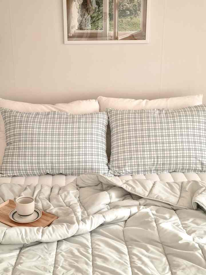 Bright white and pale green bedroom featuring checkered pillows and a natural wood tray for a cozy, clean look
