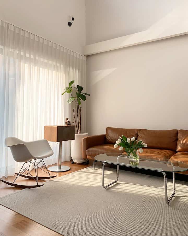 Natural color and white toned living room featuring brown leather sofa and glass coffee table in modern style