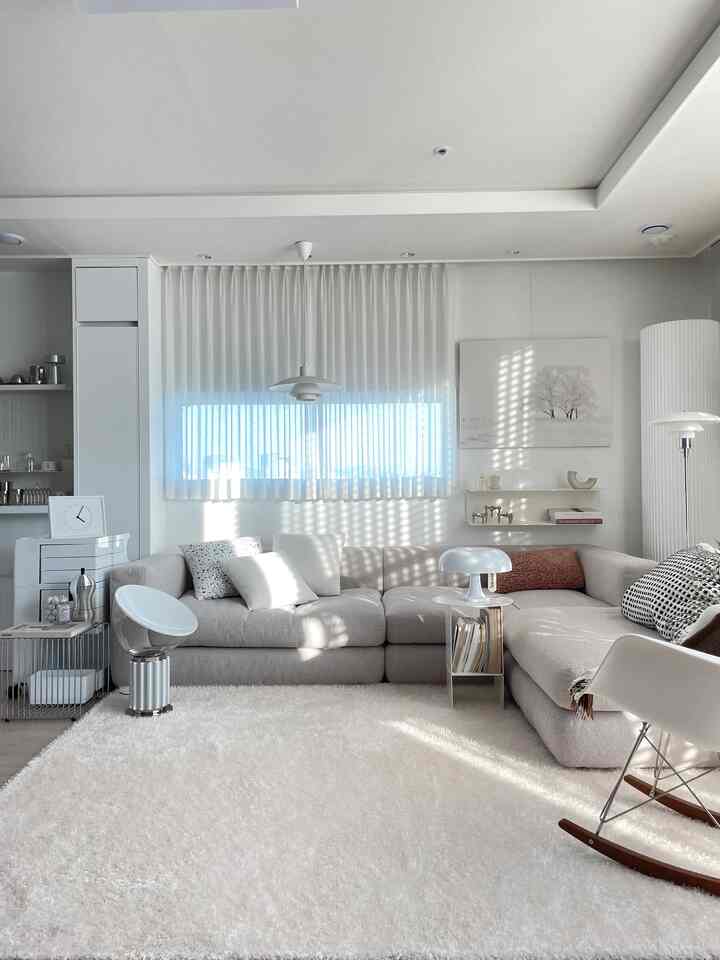 White and beige toned living room featuring large sectional sofa, rug, various lamps, and armchair in natural modern style