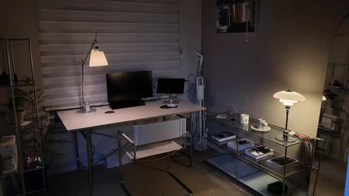 グレーの壁と白い家具が調和したモダンなホームオフィス、机と照明、棚が配置され落ち着いた雰囲気のインテリア