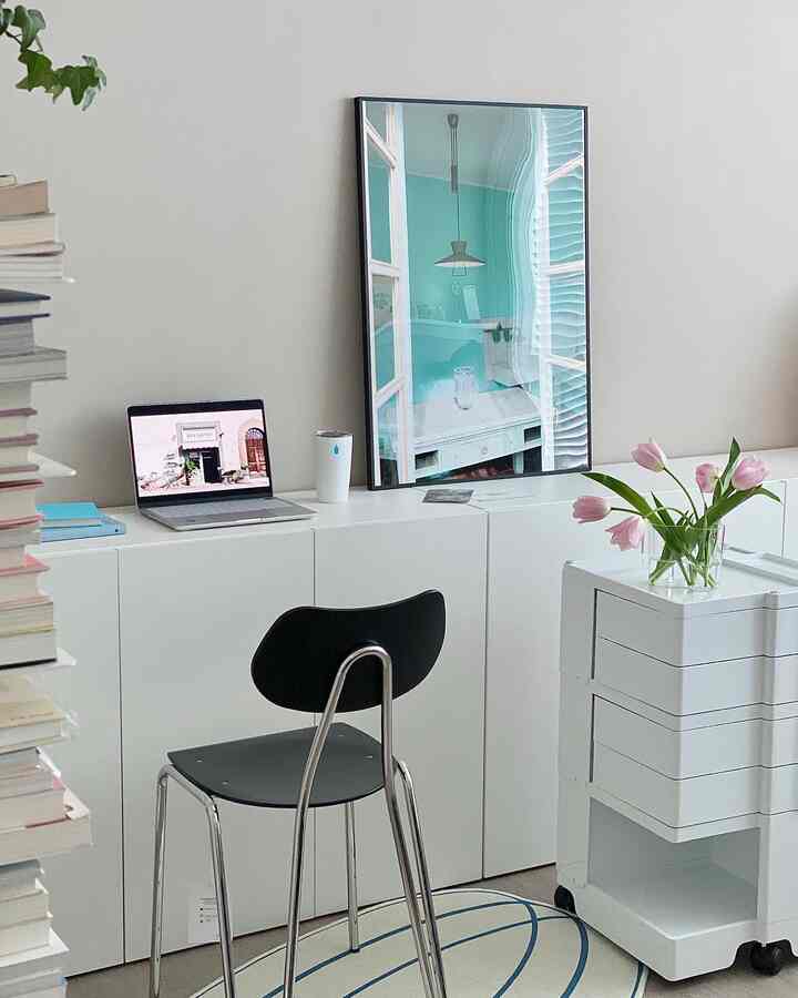 White-toned study space featuring white cabinets, a black chair, art poster, and a trolley in a clean home office setup