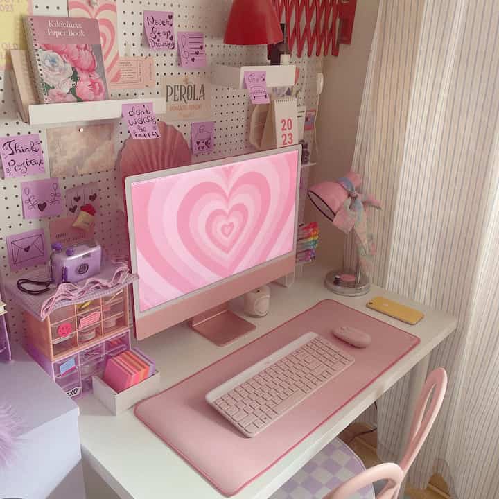Pink-toned home office space featuring a compact white desk with pink keyboard, mouse, and monitor, creating a cozy atmosphere