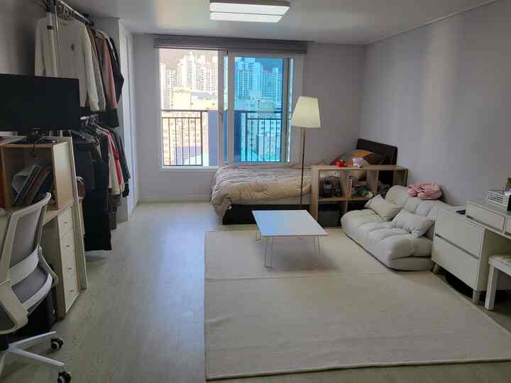 ベージュとホワイトの色調のワンルーム、ベッドとソファベッド、書棚、コーヒーテーブルが配置されたシンプルな雰囲気のインテリア