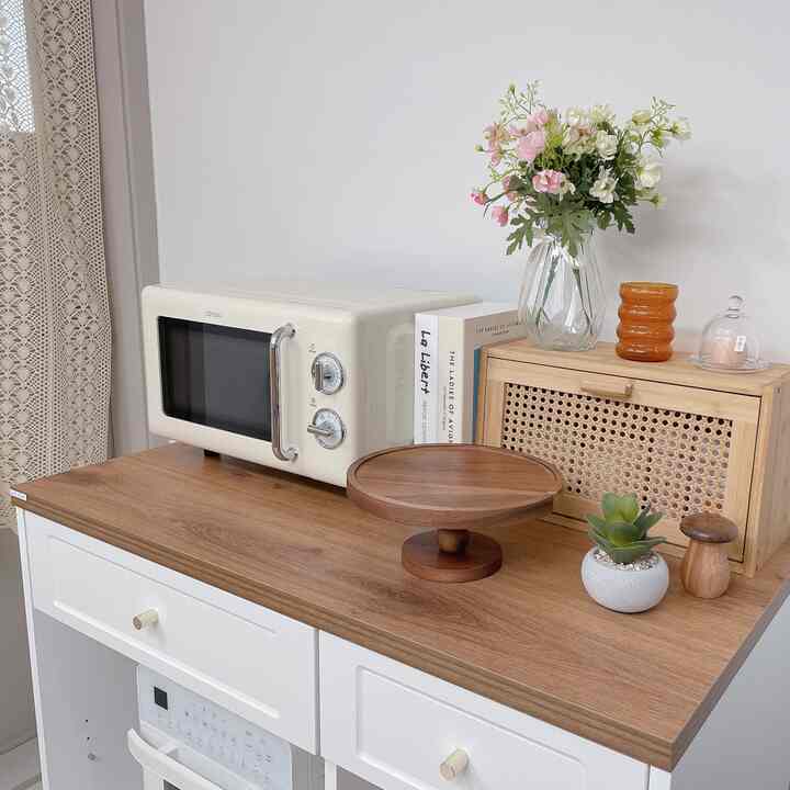 Kitchen space with white and wood tones featuring a microwave, storage cabinet, and decorative items creating a cozy atmosphere
