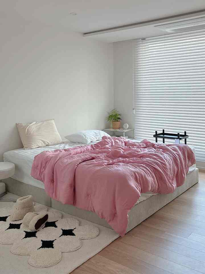 Bright modern bedroom in white and beige tones featuring a pink duvet and minimal furnishings