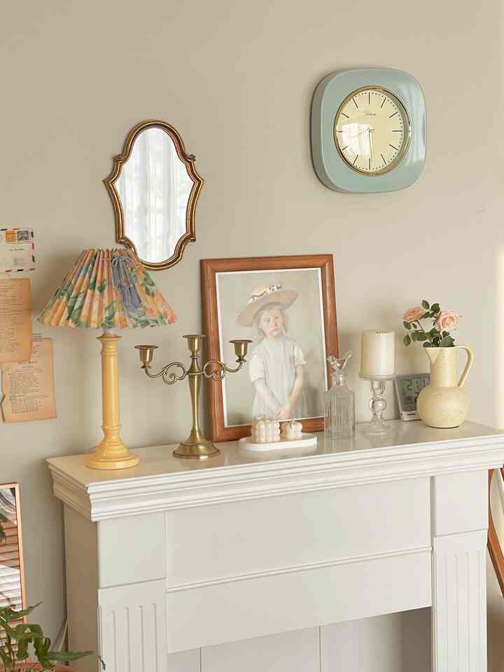 ベージュ色の壁にヴィンテージスタイルの時計、アンティークミラー、額縁の絵画、花瓶、キャンドルスタンドが配置された雰囲気のあるウォールデコ