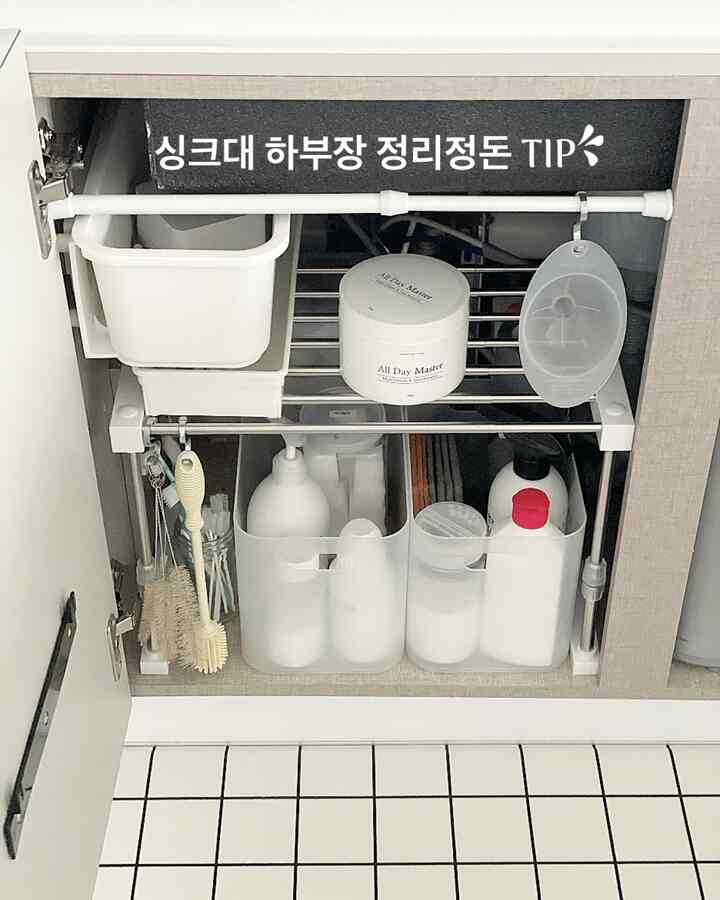 White and gray toned kitchen under-sink cabinet featuring various storage containers and adjustable shelving, neatly organized space