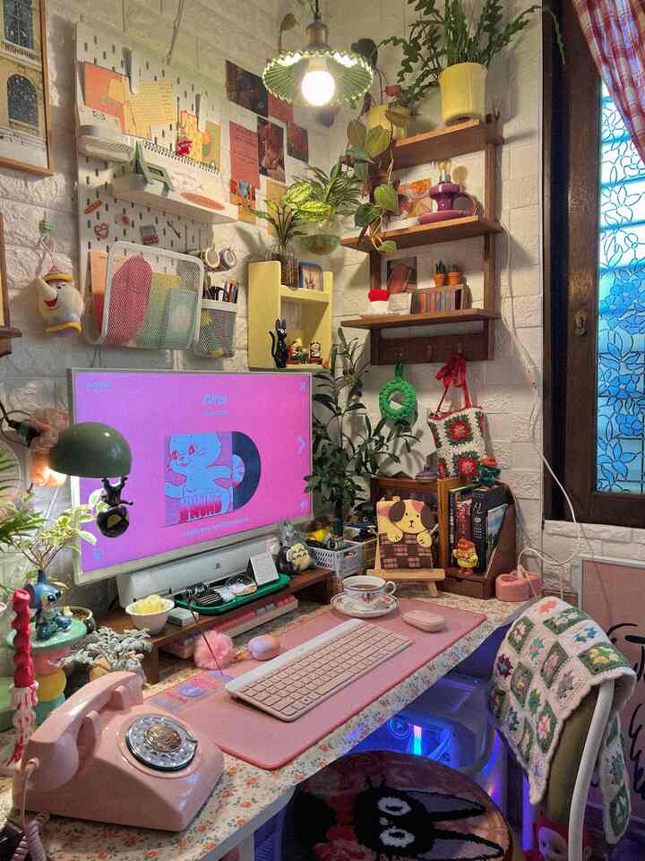 A cozy home office with a pink desk and vintage decor featuring plants and cute accessories on wall shelves and desk creating a warm atmosphere