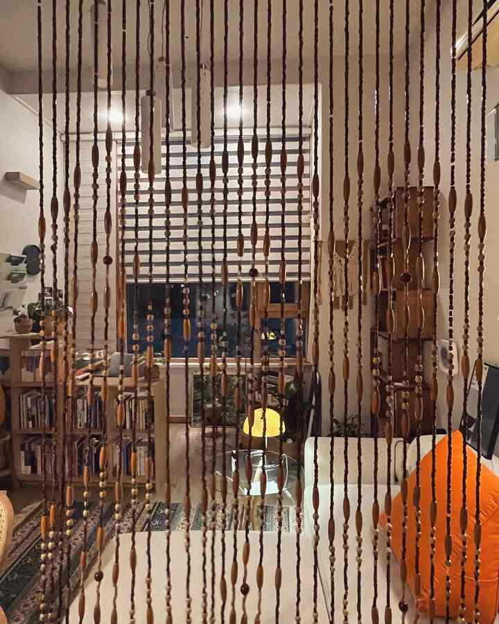 白と木目調のリビング、書棚とソファ、木製ビーズカーテンが配置された雰囲気のあるインテリア