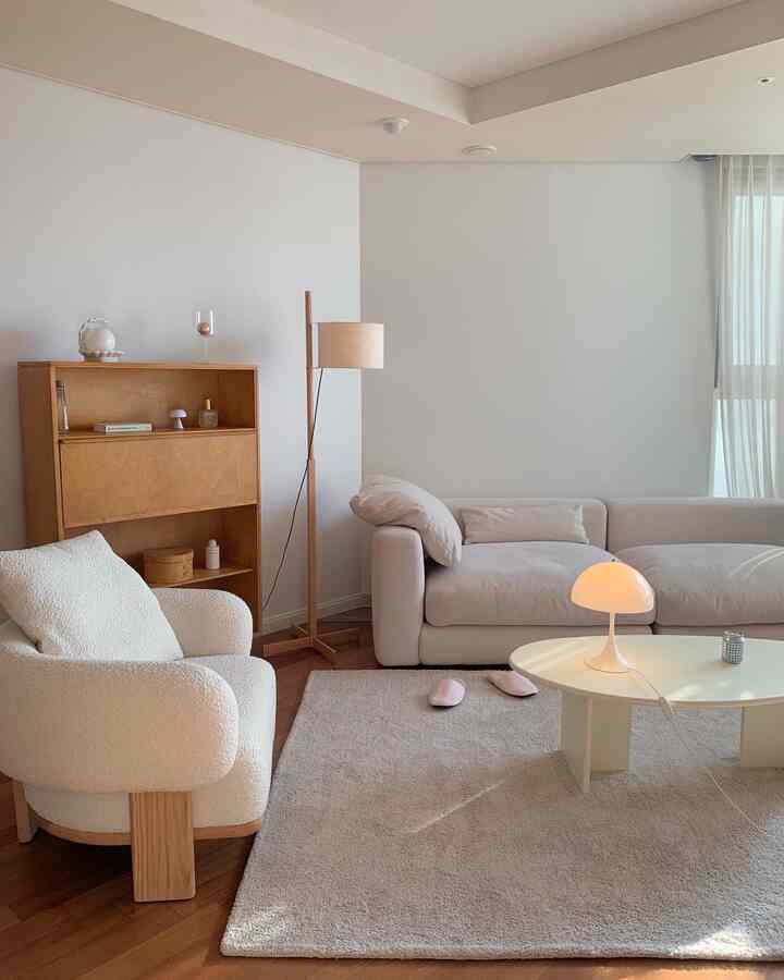 Bright white and wood-toned living room featuring soft sofa, armchair, rug, and lighting for a simple, natural atmosphere