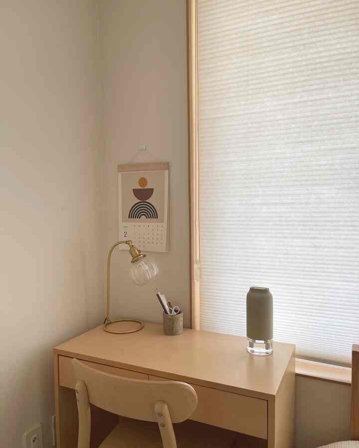 Beige and natural toned small home office featuring a simple desk, chair, minimal lamp, and white blinds creating calm atmosphere