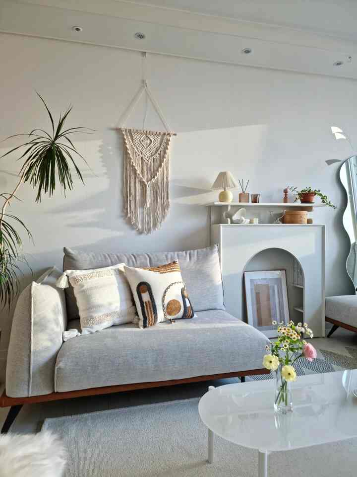 ホワイトとグレーのトーンのリビングルーム、中央にグレーのソファとクッション、暖炉コンソールと壁デコが調和した落ち着いた空間