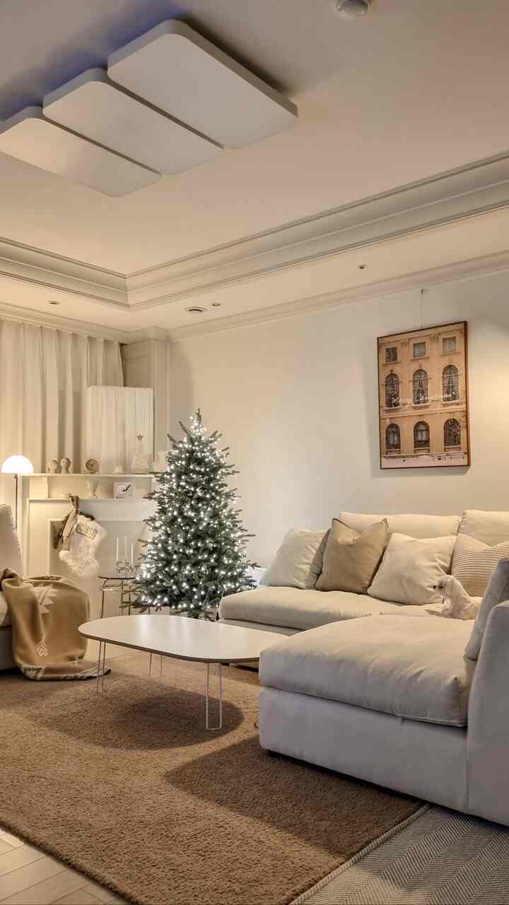 White and beige toned living room featuring a Christmas tree and large sectional sofa with a warm modern atmosphere