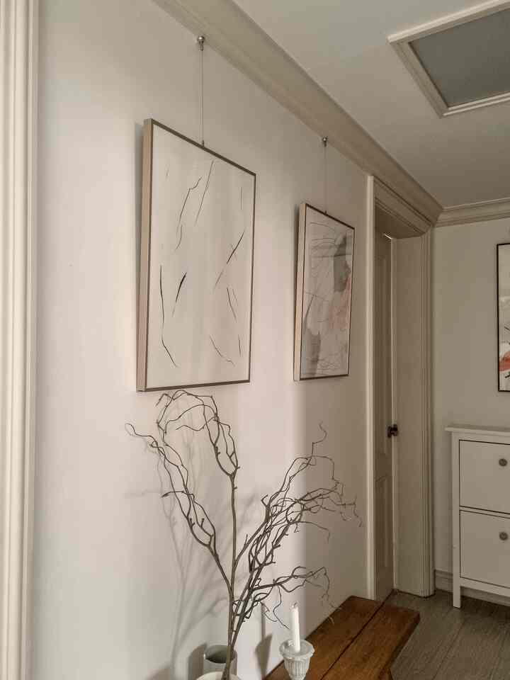 白い壁とブラウンの木製ベンチ、モダンアートの額縁ポスターが配置されたナチュラルトーンの廊下の印象的な空間