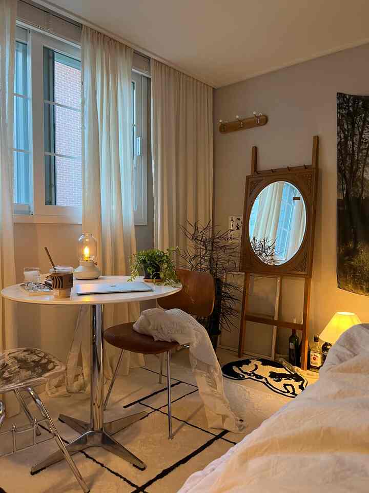 White and natural brown toned bedroom featuring a round table, wooden chair, and indoor plants creating a cozy home office atmosphere