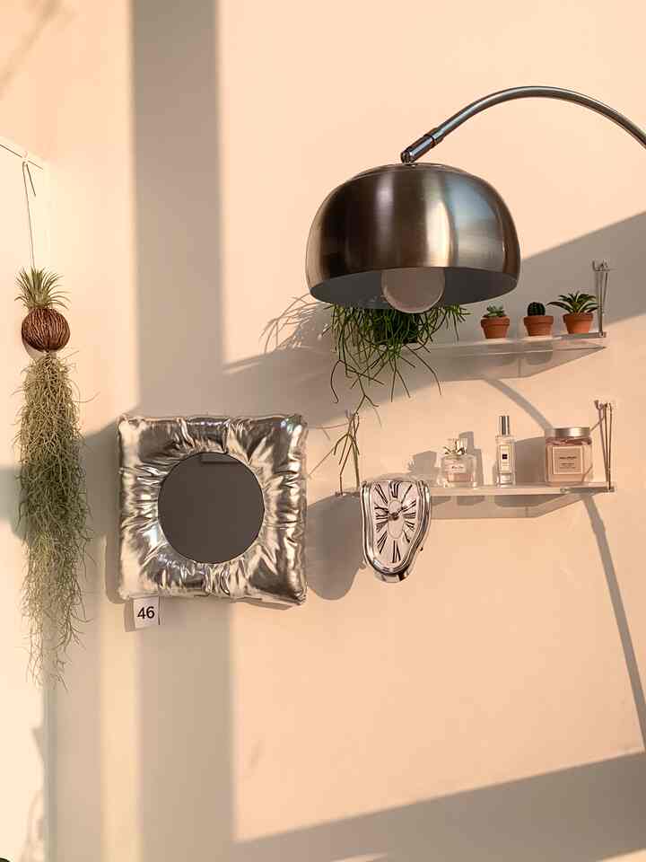 Silver-toned wall featuring a floor lamp, cushion mirror, melting clock, and small plants creating a cozy decorative interior