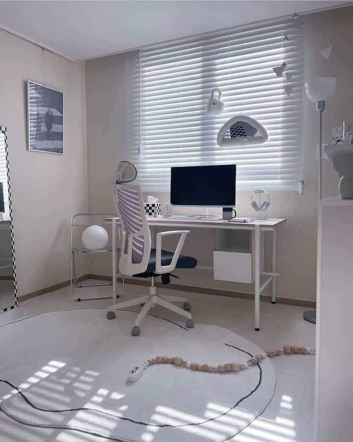White and monotone studio home office featuring desk, office chair, blinds, and large rug arranged in a neat workspace