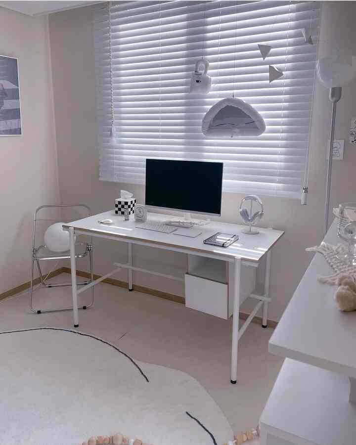 Monotone white studio home office featuring a white desk, blinds, transparent chair, and minimalist decor with organized workspace