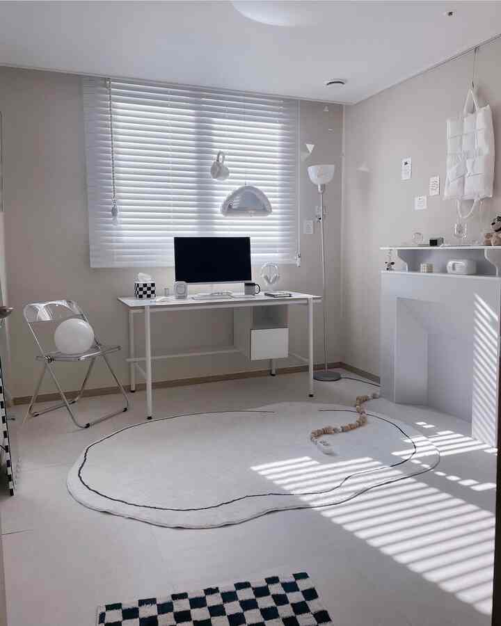 アイボリーとホワイトトーンのワンルームホームオフィス、シンプルなデスクと透明な椅子、ミッドセンチュリーモダンの照明とラグが調和した雰囲気のあるインテリア