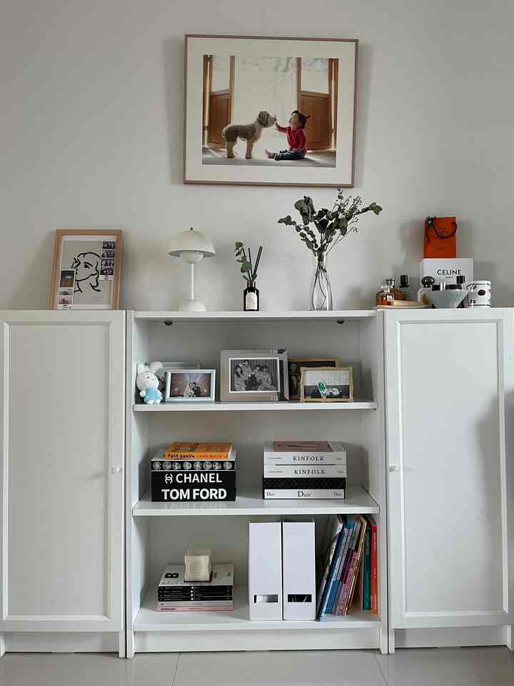 Natural-toned living space featuring white BILLY bookshelf with picture frames, lamp, and plant arranged neatly